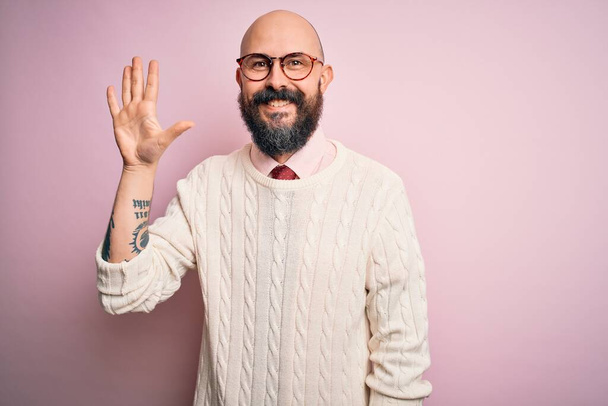 Handsome bald man with beard and tattoo wearing glasses and sweater over pink background showing and pointing up with fingers number five while smiling confident and happy. - Photo, Image