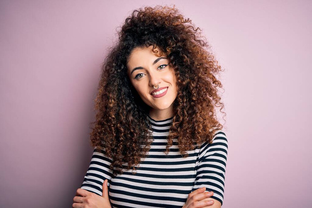 Young beautiful woman with curly hair and piercing wearing casual striped t-shirt happy face smiling with crossed arms looking at the camera. Positive person. - Photo, Image