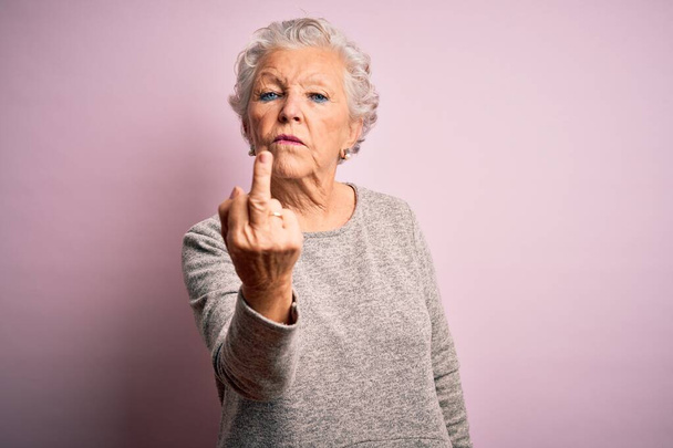 Старшая красивая женщина в повседневной футболке стоит на изолированном розовом фоне показывая средний палец, невежливый и грубый отъебись выражение лица
 - Фото, изображение