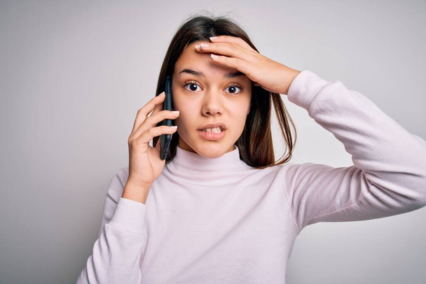 Beautiful brunette girl having conversation talking on the smartphone over white background stressed with hand on head, shocked with shame and surprise face, angry and frustrated. Fear and upset for mistake. - Photo, Image