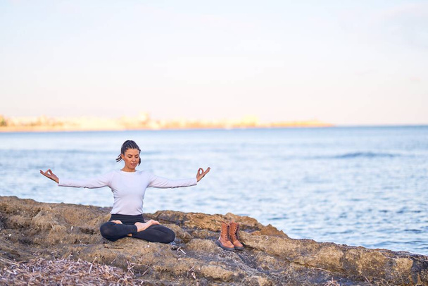 junge schöne Sportlerin praktiziert Yoga. Trainer bringt Lotus-Pose am Strand bei - Foto, Bild