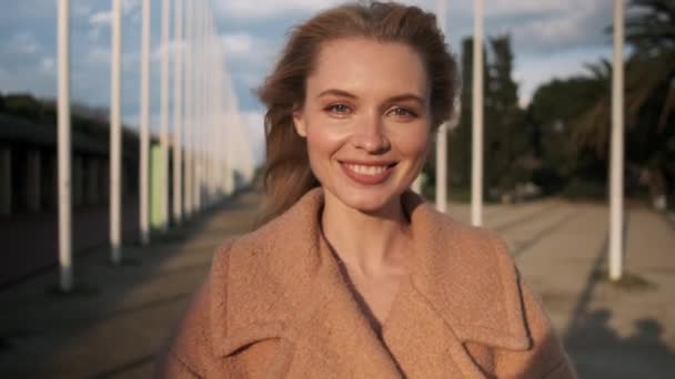 Portret van mooi blond meisje glimlachend en gelukkig kijkend in camera op straat bij zonsondergang - Video