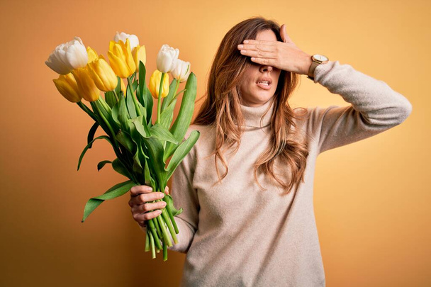 Joven mujer morena hermosa sosteniendo ramo de tulipanes amarillos sobre fondo aislado cubriendo los ojos con la mano, mirando grave y triste. Indiferente, ocultamiento y rechazo
 - Foto, Imagen