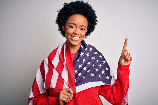 Kıvırcık saçlı, Amerika Birleşik Devletleri bayrağı taşıyan genç Afrikalı Afro kadın bir fikir ya da soruyla şaşırdı ve mutlu bir yüzle işaret etti. - Fotoğraf, Görsel
