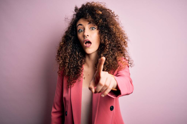 Young beautiful businesswoman with curly hair and piercing wearing elegant jacket pointing displeased and frustrated to the camera, angry and furious with you - Foto, Imagem