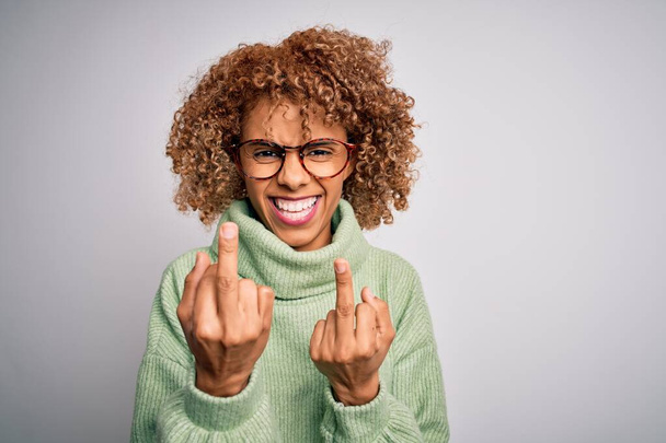 Young beautiful african american woman wearing turtleneck sweater and glasses Showing middle finger doing fuck you bad expression, provocation and rude attitude. Screaming excited - Foto, afbeelding