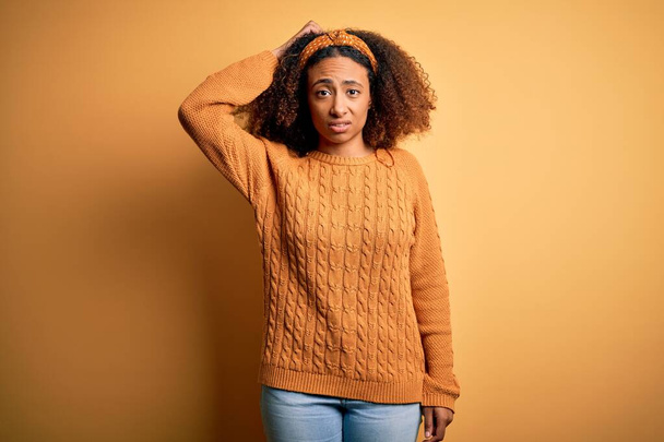 Mujer afroamericana joven con el pelo afro usando suéter casual sobre fondo amarillo confundir y preguntarse acerca de la pregunta. Incierto con la duda, pensando con la mano en la cabeza. Concepto pensativo
. - Foto, imagen