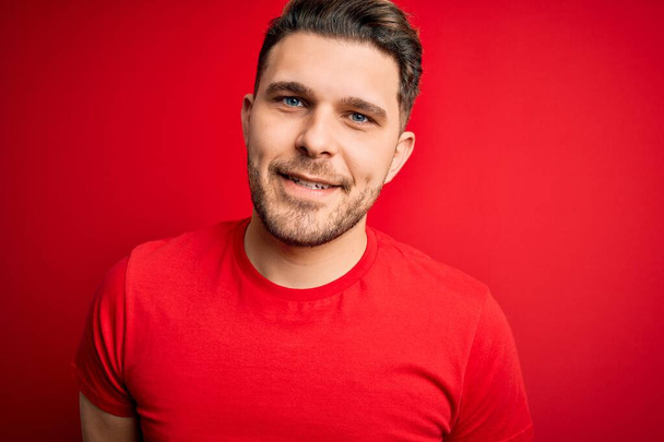 Young man with blue eyes wearing casual t-shirt over red isolated background with a happy and cool smile on face. Lucky person. - Fotó, kép