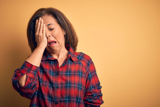 Middle age beautiful woman wearing casual shirt standing over isolated yellow background Yawning tired covering half face, eye and mouth with hand. Face hurts in pain. - Photo, Image