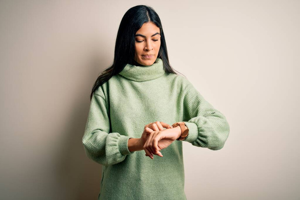 Mladá krásná hispánská žena na sobě zelené zimní svetr na izolovaném pozadí Kontrola času na hodinky na zápěstí, uvolněné a sebevědomé - Fotografie, Obrázek