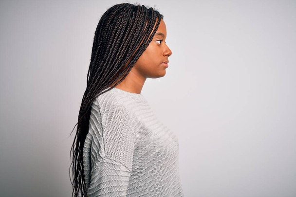 Молодая африканская американка стоит случайный и прохладный на сером изолированном фоне глядя в сторону, расслабиться профиль позировать с естественным лицом с уверенной улыбкой
. - Фото, изображение