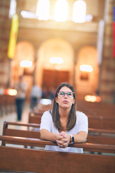 Jovem mulher bonita orando de joelhos em um banco na igreja
 - Foto, Imagem