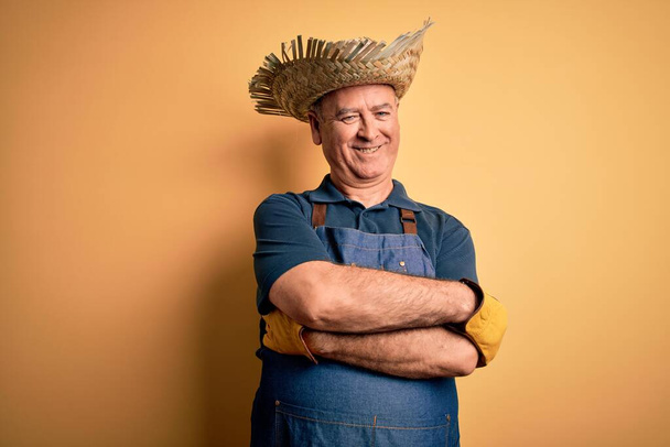 Middle age hoary farmer man wearing apron and hat over isolated yellow background happy face smiling with crossed arms looking at the camera. Positive person. - Fotografie, Obrázek