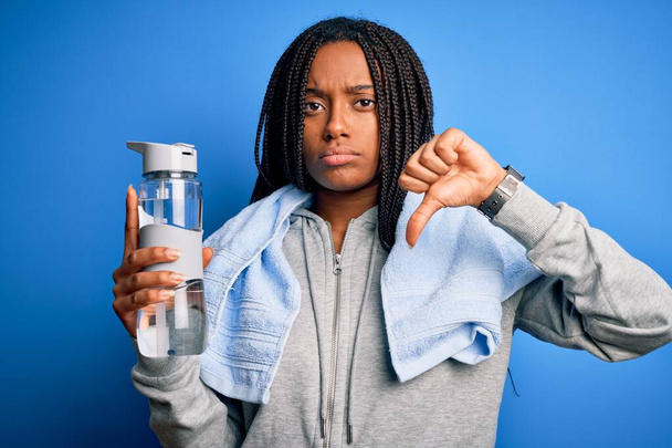 Genç Afrikalı Amerikalı spor kadın kazak giyiyor ve kızgın yüzlü içme suyu içiyor, negatif işaret baş parmakları aşağıda, reddedilme konsepti var. - Fotoğraf, Görsel