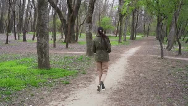 Attractive Caucasian woman wear protective medical face mask, warm jacket calmly walk along path among trees, suddenly spins around. Happy girl starts jumping, dancing in empty forest in cold morning. - Footage, Video