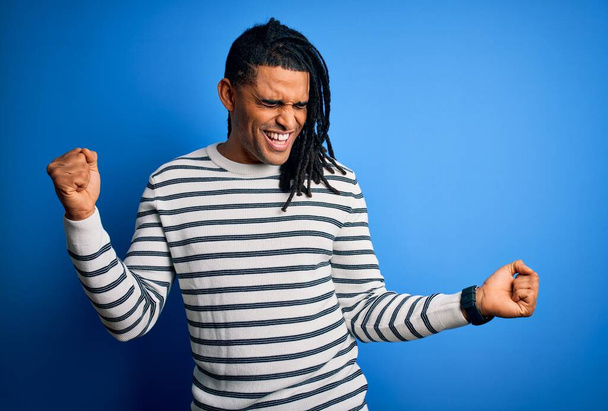 Young handsome african american afro man with dreadlocks wearing casual striped sweater Dancing happy and cheerful, smiling moving casual and confident listening to music - Photo, Image