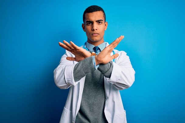 Handsome african american doctor man wearing coat and stethoscope over blue background Rejection expression crossing arms doing negative sign, angry face - Foto, Bild