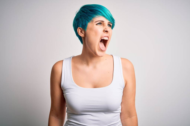 Jonge mooie vrouw met blauwe mode haar dragen casual t-shirt over witte achtergrond boos en gek schreeuwen gefrustreerd en woedend, schreeuwen van woede. Woede en agressief concept. - Foto, afbeelding