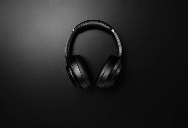 Black headphones on black matte background. Minimalistic composition top view. Bluetooth headphones - Photo, Image