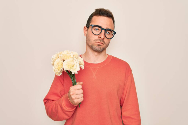 Mavi gözlü genç bir adam beyaz arka planda çiçek buketi tutuyor. Akıllı yüzünde kendine güvenen bir ifade var ve ciddi düşünüyor. - Fotoğraf, Görsel