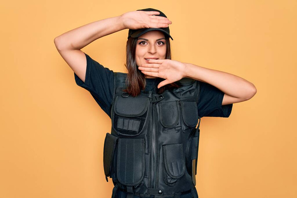 Nuori kaunis brunette poliisi nainen yllään poliisin yhtenäinen luodinkestävä ja korkki Hymyilevä iloinen pelaa kurkistaa boo kädet osoittavat kasvot. Yllätys ja poistuminen
 - Valokuva, kuva