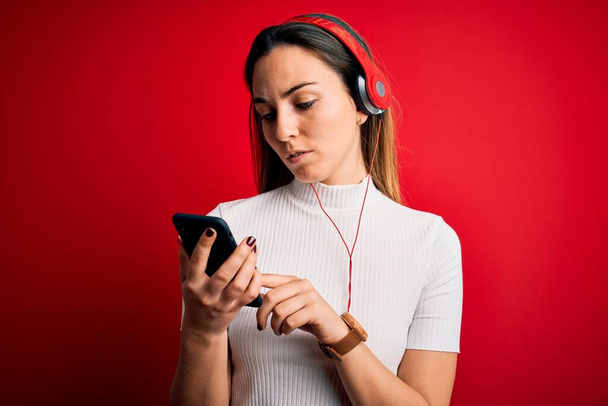 Молодая красивая брюнетка слушает музыку с помощью смартфона и наушников с уверенным выражением на умном лице, думая серьезно
 - Фото, изображение