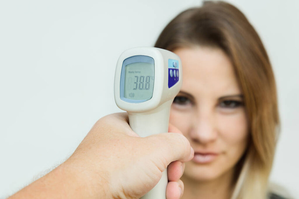 Использование инфракрасного бесконтактного термометра на лбу для проверки температуры тела на наличие симптомов вирусного ковида-19
 - Фото, изображение