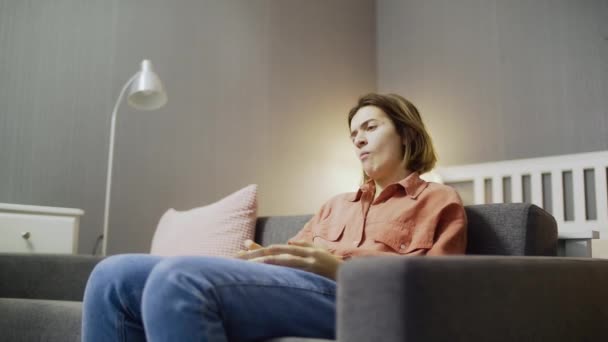 Dissatisfied and disappointed woman sitting on the sofa, watching TV and throwing popcorn - Footage, Video