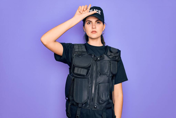 Jovem polícia mulher vestindo uniforme colete à prova de balas de segurança sobre fundo roxo zombando de pessoas com os dedos na testa fazendo gesto perdedor zombando e insultando
. - Foto, Imagem