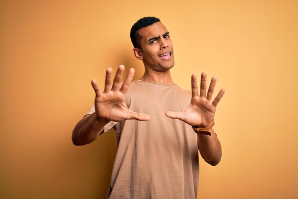 Junge gutaussehende afrikanisch-amerikanische Mann in lässigem T-Shirt vor gelbem Hintergrund Angst und Schrecken mit Angst Ausdruck Stop-Geste mit den Händen, schreien vor Schreck. Panikkonzept. - Foto, Bild