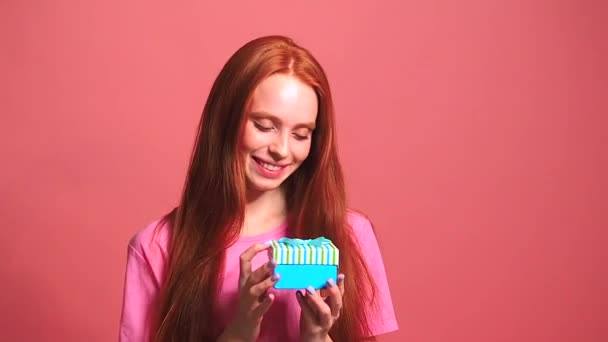 beautiful redhaired ginger woman in pink studio background unpacking the box - Filmati, video