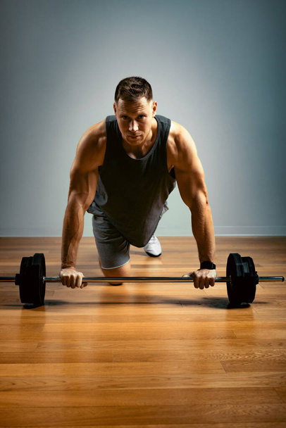 Een man doet oefeningen met een lange halter op een grijze achtergrond. Fitness concept, sportieve motivatie. - Foto, afbeelding