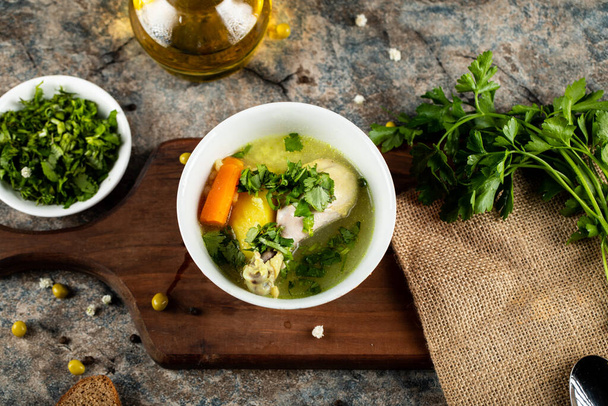 Бульон суп с морковью, картофелем и мясной зеленью на деревянной доске подается с зеленым салатом
 - Фото, изображение