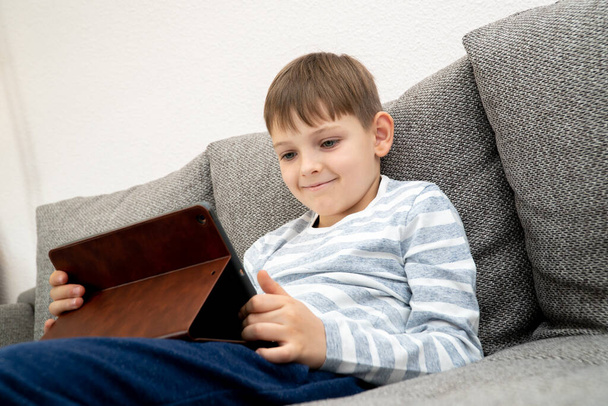 Looking up young boy thinking in front of tablet pc. Distance learning online education. Cute caucasian boy doing homework at home while quarantine of pandemia coronavirus - Foto, imagen
