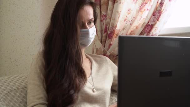 Close up businesswoman in protective medical face mask remote work on laptop online at home. Brunette girl typing response to client on notebook keyboard. Successful lady surf internet on computer. - Кадры, видео
