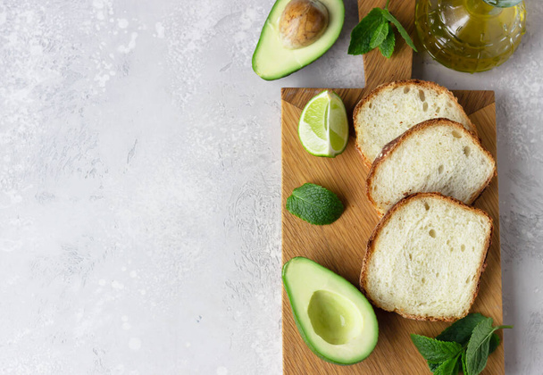 Sliced homemade no knead bread on wooden cutting board with avocado. The concept of homemade bakery without yeast. Light grey stone background. Top view. - Photo, Image