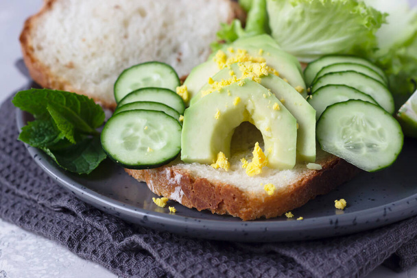 Healthy vegetarian sandwich with no knead homemade bread, avocado and cucumbers for breakfast or lunch. Light grey stone background.  - Photo, Image