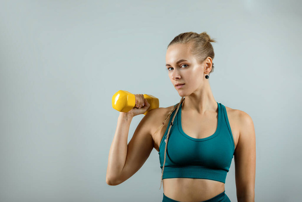 Beautiful fitness model doing exercises with dumbbells in hands on a gray background. Close-up. Woman posing on camera with dumbbells. Healthy lifestyle. Achieving goals, sports motivation. Copy space - Foto, imagen