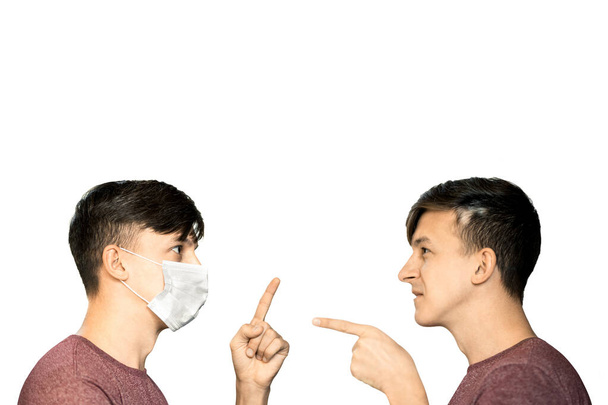 Temat ochrony przed koronawirusem. Dwóch identycznych młodych mężczyzn w masce wirusa i bez niej, pokazać palce z zagrożeniem dla siebie nawzajem. - Zdjęcie, obraz