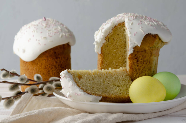 Kulich Easter cake with colored eggs with white glaze on white wooden background - Fotó, kép