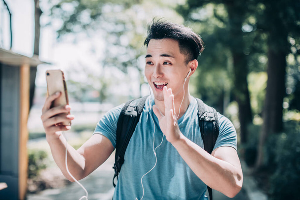 Mutlu genç adam sokakta yürüyor ve cep telefonu kullanıyor. - Fotoğraf, Görsel