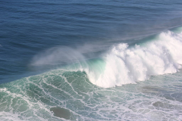 Surfers and the giant waves of Nazar, in Portugal, can be seen from the "Canhao de Nazare". - Photo, Image