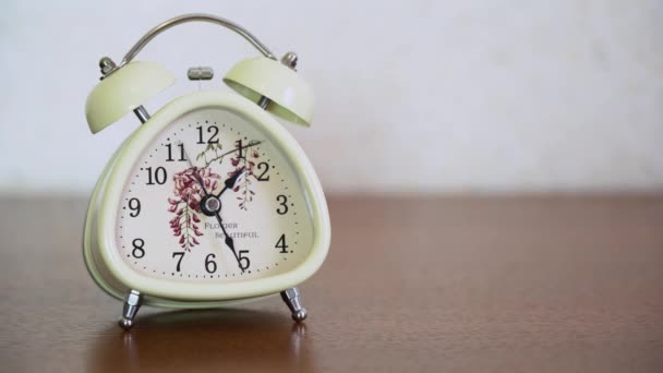 Weißer Retro-O-Clock-Wecker mit Glöckchen steht auf einem braunen Holztisch vor verschwommenem Hintergrund in Großaufnahme mit Kopierraum. Stil klassische alte Glocke zeigen etwa 13.25 Uhr Ortszeit im Haus. - Filmmaterial, Video