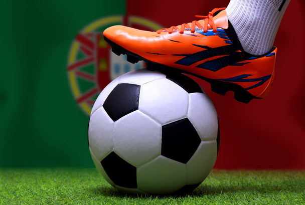 Крупным планом ноги футболиста или футболиста ходят по зеленой траве, готовые к матчу на фоне национального флага Португалии
. - Фото, изображение