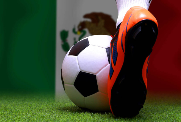 Κλείστε τα πόδια και τα πόδια του ποδοσφαιριστή ή ποδοσφαιριστή με τα πόδια σε πράσινο γρασίδι έτοιμο να παίξει αγώνα σε εθνικό φόντο σημαία του Μεξικού. - Φωτογραφία, εικόνα