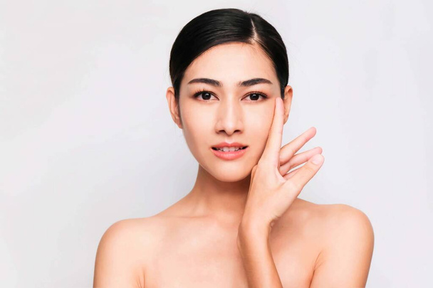 junge schöne asiatische Frau mit sauberer und heller Haut, kosmetisches Schönheitskonzept, Hände berühren sich auf der Wange, lächelndes und freundliches Gesicht isoliert auf grauem Hintergrund - Foto, Bild