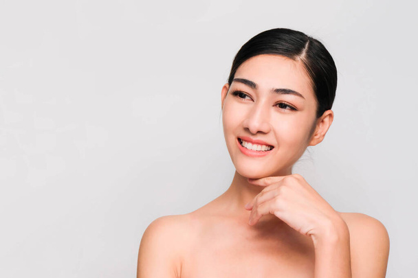 young beautiful asian woman with clean and bright skin, Cosmetic Beauty Concept,hands touch on the cheek, smiling and friendly face isolated on grey background - Foto, immagini