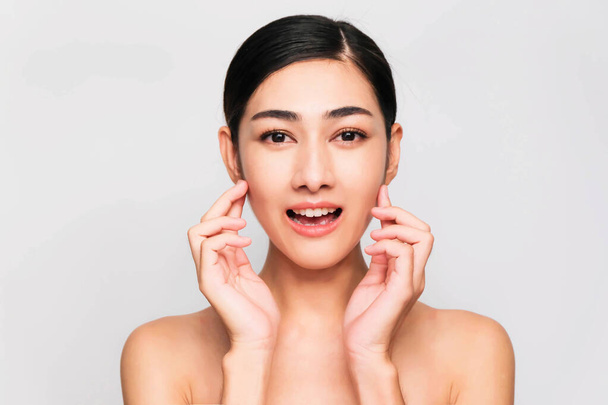 young beautiful asian woman with clean and bright skin, Cosmetic Beauty Concept,hands touch on the cheek, smiling and friendly face isolated on grey background - Zdjęcie, obraz