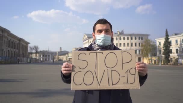  Modern férfi orvosi maszkban kérje, hogy állítsa meg a járványt COVID 19 poszterrel a város utcáján.  - Felvétel, videó