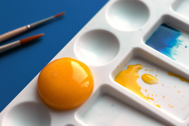 White palette with watercolor paints on a trendy classic blue background. Vmseto yellow paint used egg yolk. Witty and design. Top view, flat lay. - Fotografie, Obrázek